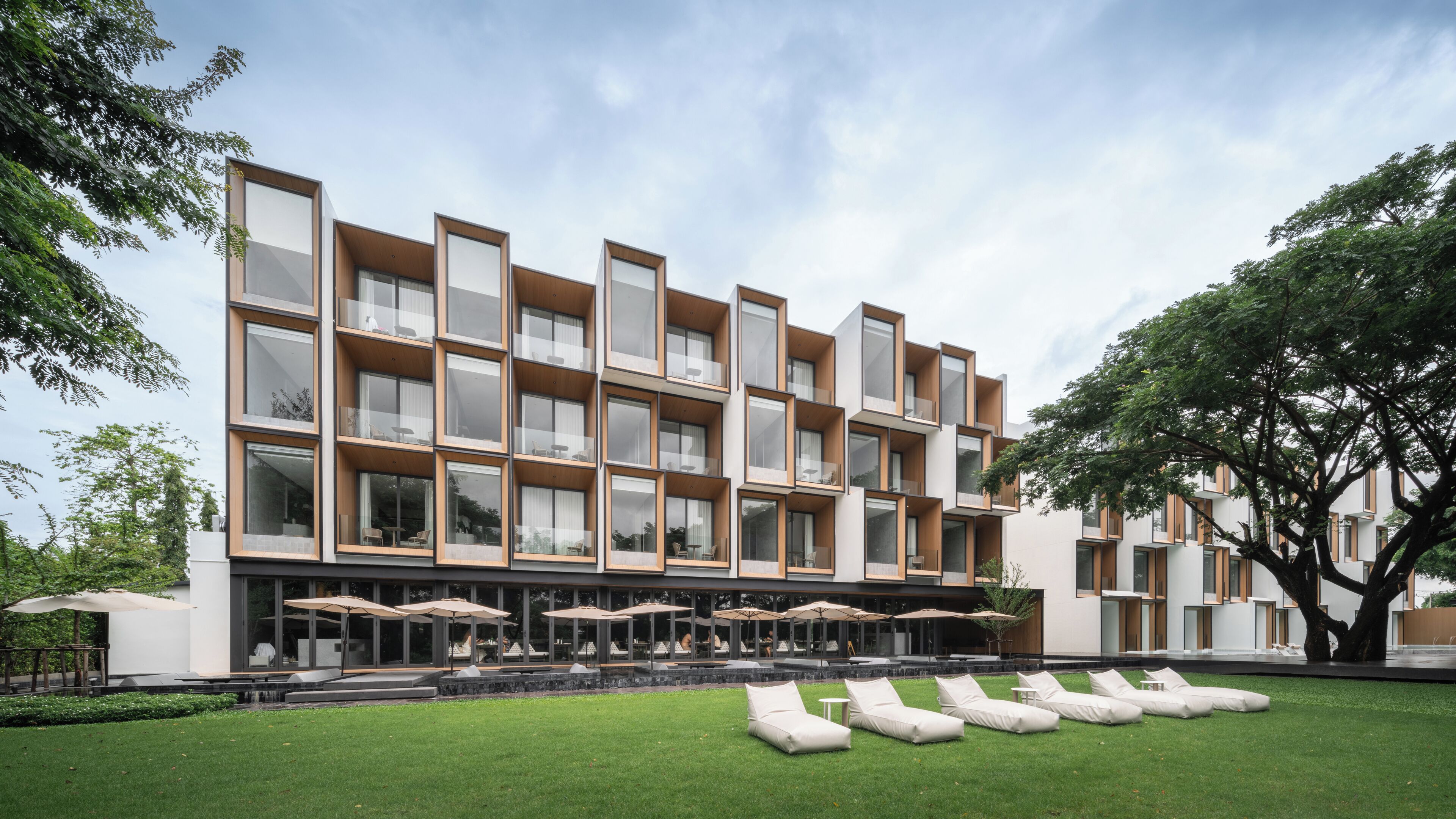 A modern hotel with multiple balconies, outdoor seating, and a well-maintained lawn.
