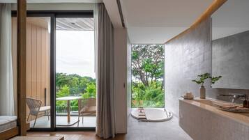 Un baño moderno con bañera, lavamanos y ventana con vistas a la vegetación.