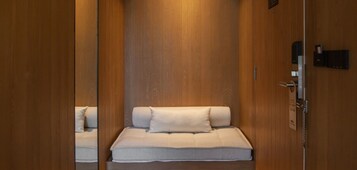 Una habitación estrecha con paneles de madera, una cama individual y una mesita de noche pequeña.