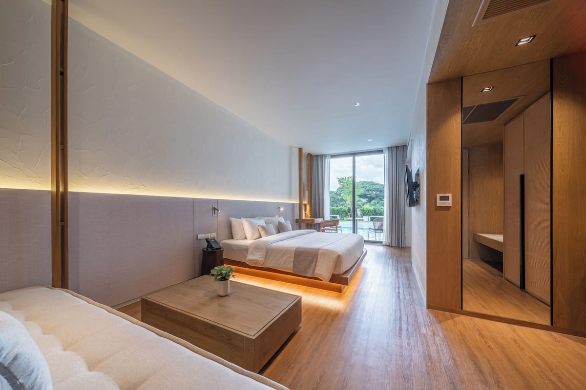 A modern hotel room with a large bed, a bedside table, and a view of the outdoors.