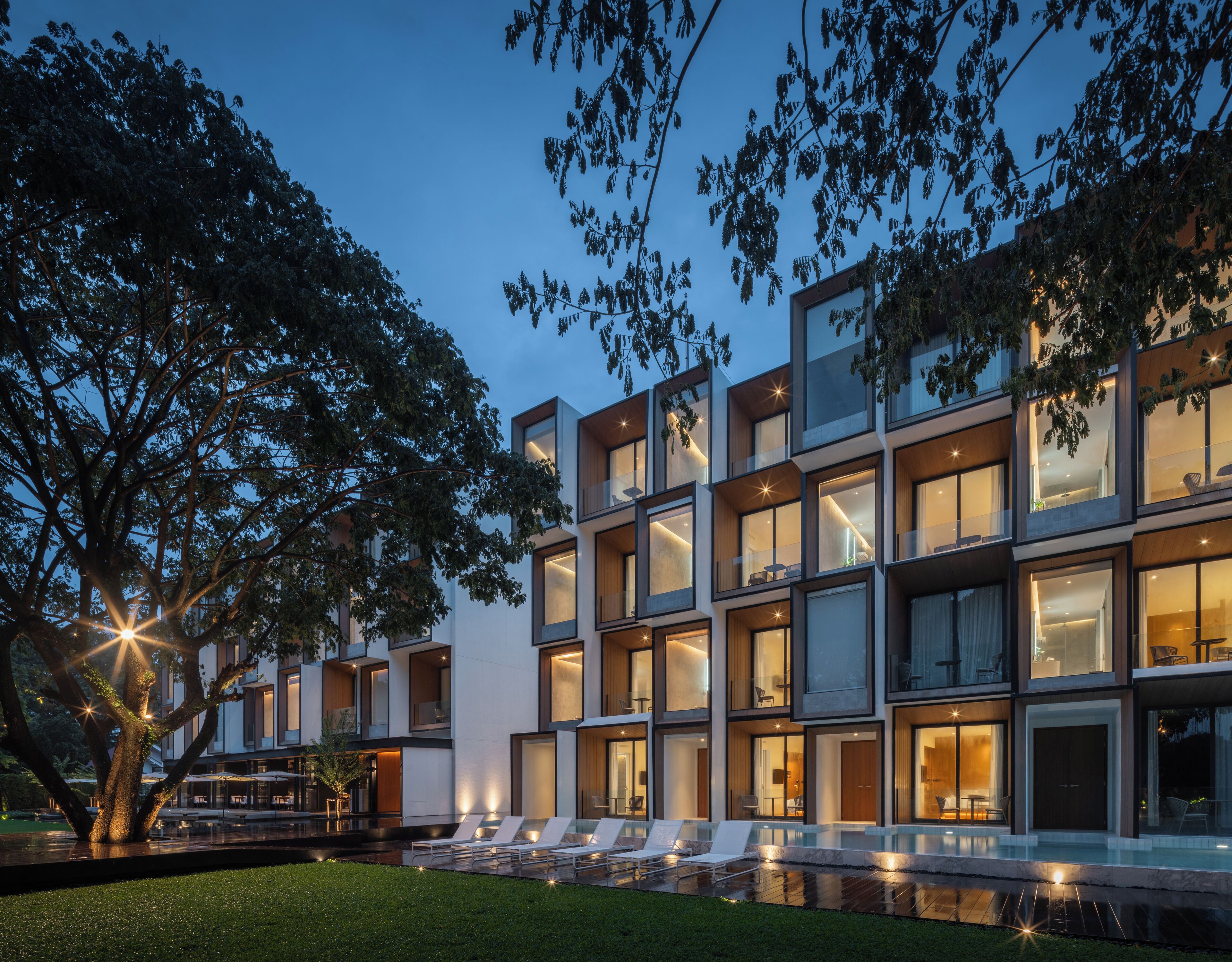 A modern multi-story building with large windows and balconies, a swimming pool, and a well-maintained lawn.