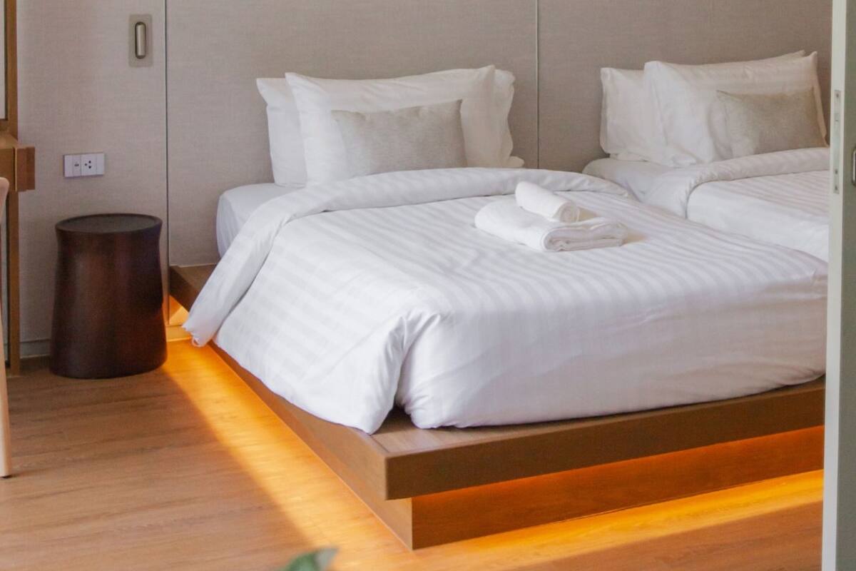 A modern hotel room with a large bed, a wooden bedside table, and a small trash bin.