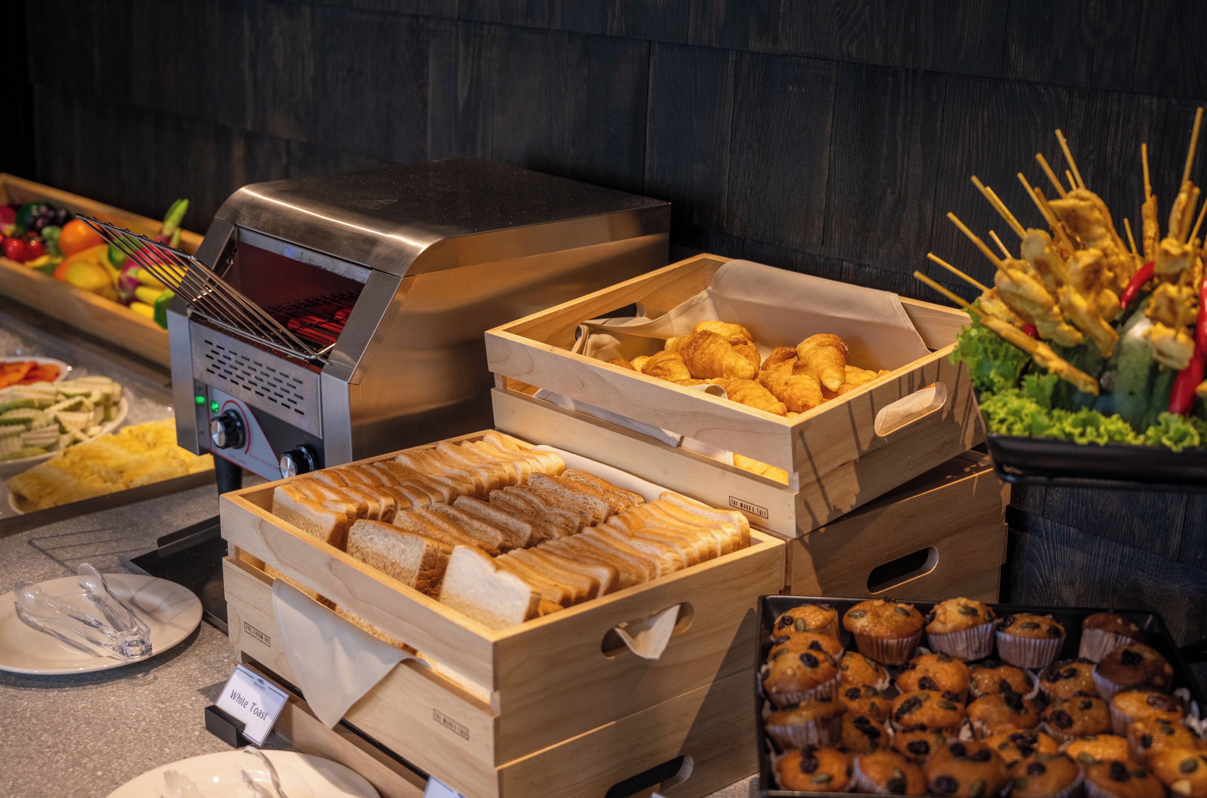 A buffet with various food items including bread, muffins, and skewers.