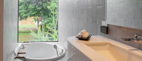 A modern bathroom with a large bathtub, a shower, and a view of a garden through a large window.