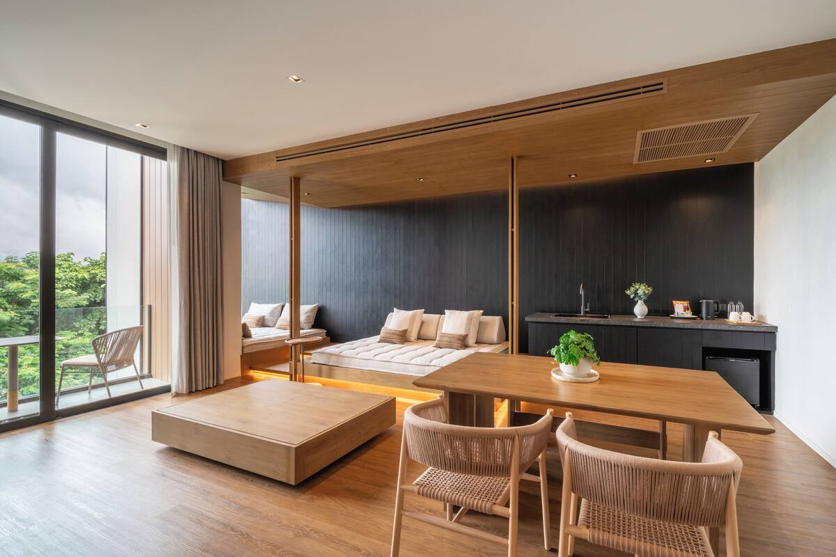 A modern living room with a wooden dining table, two sofas, and a large window offering a view of greenery.