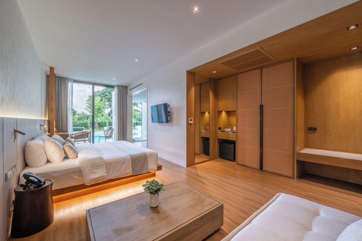 A modern hotel room with a bed, a small table with a plant, a TV mounted on the wall, and a wooden wardrobe.
