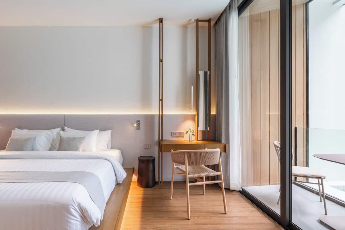 A modern hotel room with a large bed, a desk, and a chair. There is a window with a view of the outside.