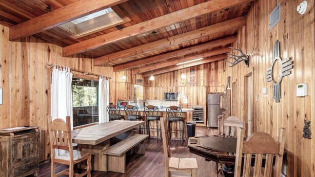 L’intérieur d’un chalet en bois rustique comprend un coin repas, une cuisine et une grande fenêtre qui laisse entrer la lumière naturelle.