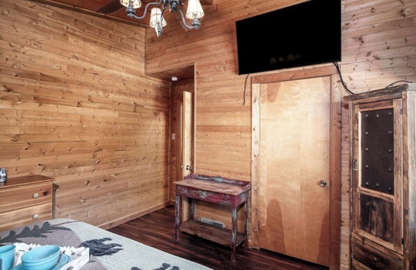 A wooden room with a bed, dresser, and a television mounted on the wall.