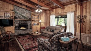 L’intérieur chaleureux d’un chalet avec une cheminée en pierre, des murs en bois, un canapé en cuir et un plafond en bois rustique.