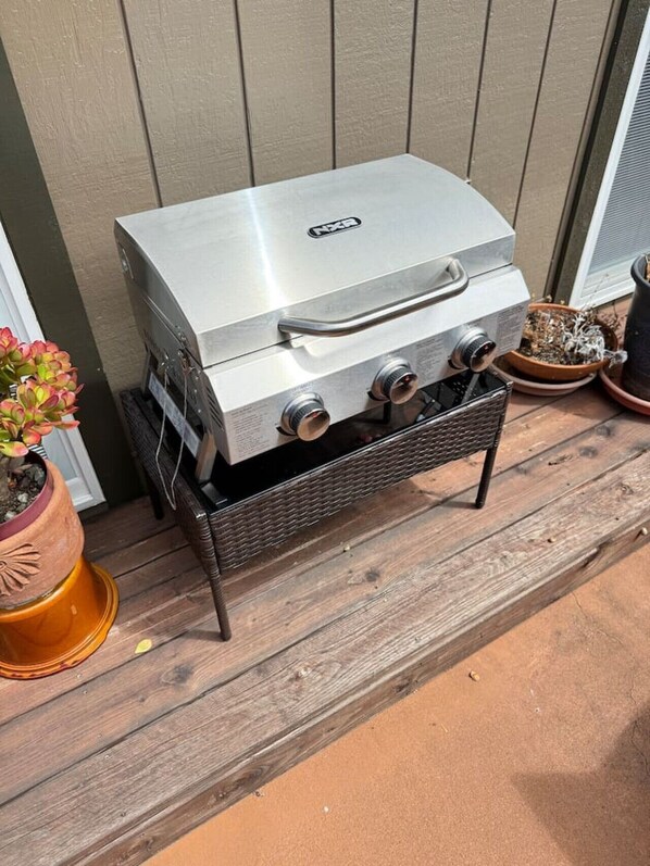 A stainless steel outdoor grill with a handle, placed on a wooden deck.