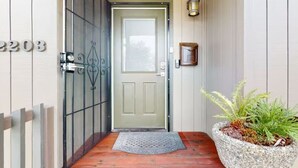 Une porte en bois avec une plaque portant un numéro, un portail en métal, un pot de fleurs et un paillasson.