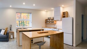A modern kitchen with a central island, white cabinetry, and a window with a view of autumn trees. - Le Camp Caché Shefford (Shefford)