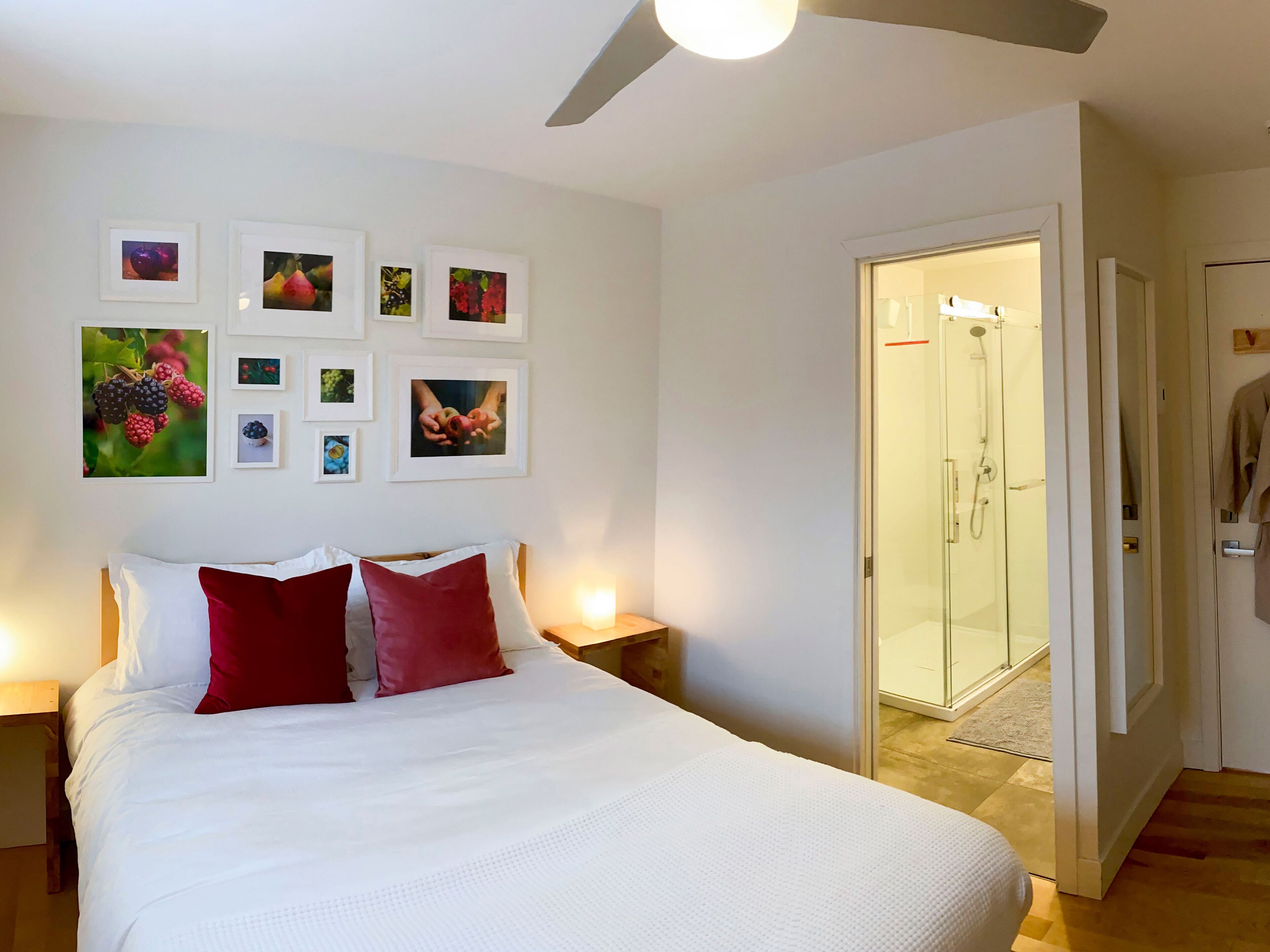 A bedroom with a bed, red pillows, a nightstand, and a wall with framed pictures.