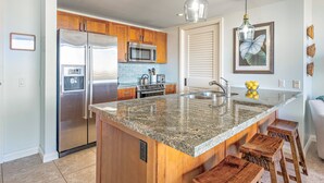 A modern kitchen with granite countertops, stainless steel appliances, wooden cabinets, and a large island with bar stools.