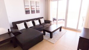 A modern living room with a dark sofa, a coffee table, and a TV stand. There are three wall-mounted artworks above the sofa.