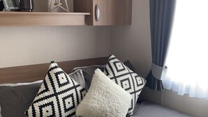 Un intérieur de camping-car chaleureux et accueillant, avec un lit, des oreillers, une décoration en forme d’étoile et une étagère sur laquelle sont posés un cadre photo et une bougie.