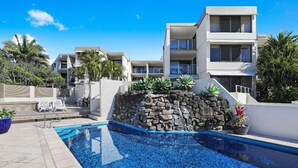 A modern hotel with a swimming pool, stone wall, and palm trees.