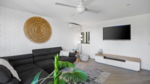 A modern living room with a black sofa, a woven wall hanging, a ceiling fan, a TV, and a console table.
