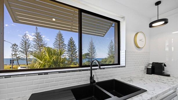 A modern kitchen with a large window, a black sink, and a coffee machine.