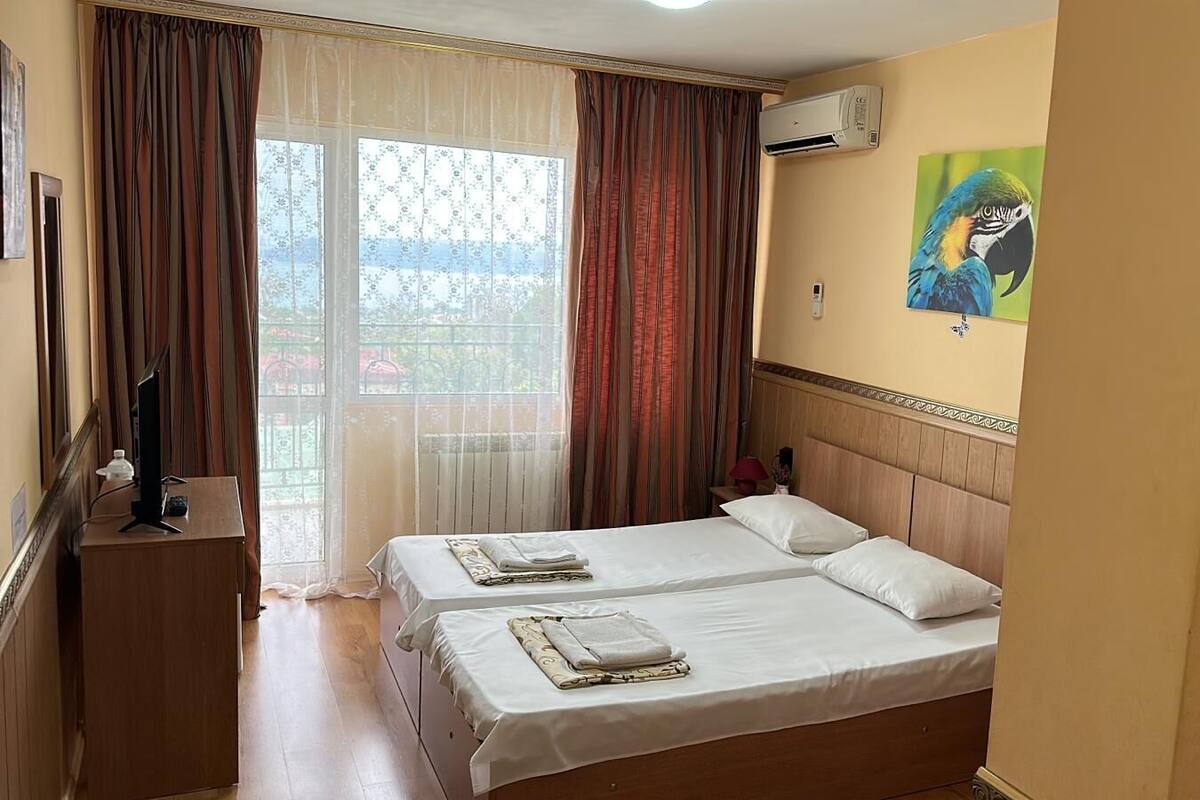 A hotel room with two beds, a desk, an air conditioner, and a painting on the wall.