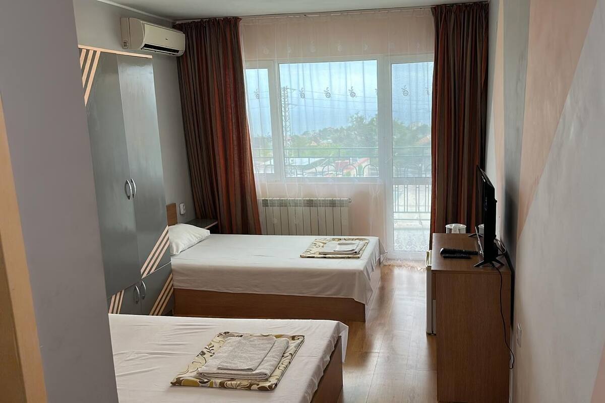 A hotel room with two beds, a TV, and a window with curtains.