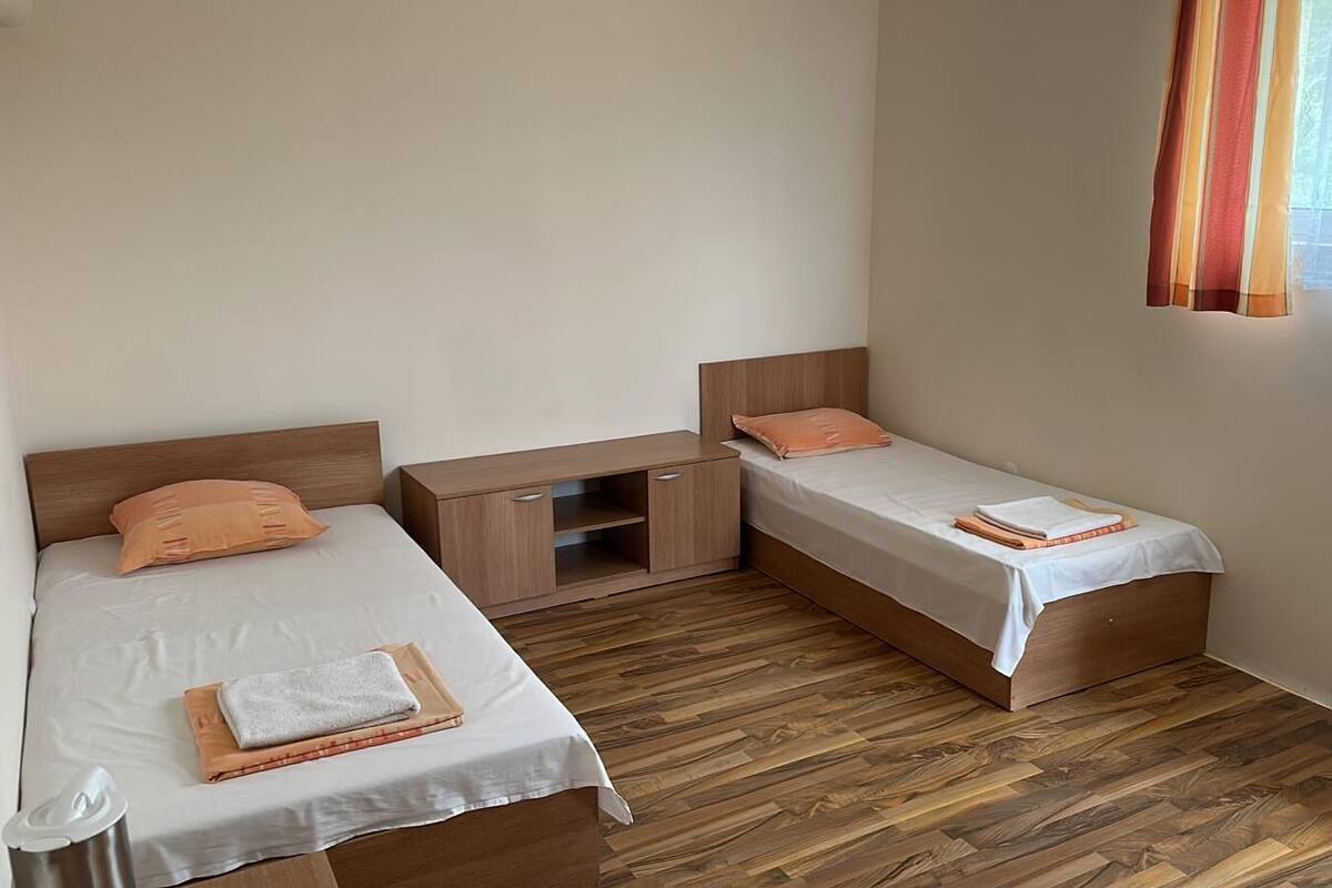 A small, clean room with two single beds, a wooden nightstand, and a white wardrobe.
