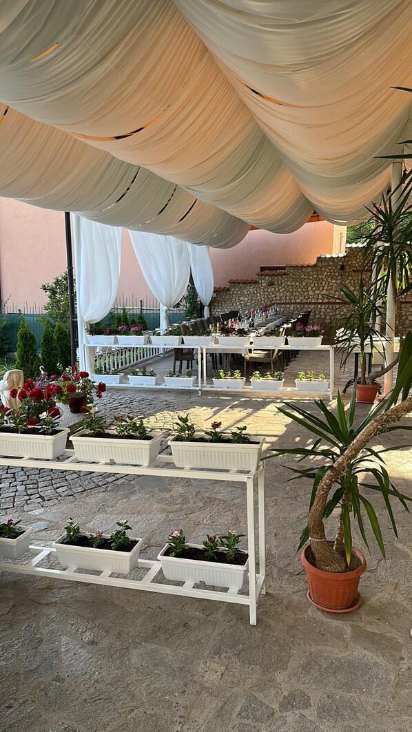 An outdoor patio with white canopies, stone flooring, and potted plants.