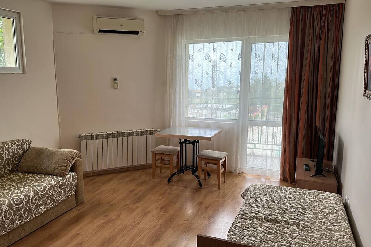 A room with a sofa, a small table with two chairs, a radiator, and a window with curtains.