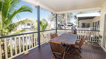 Relax on the covered deck with a wooden table and chairs, surrounded by a picket fence and a clear view of the surrounding area.