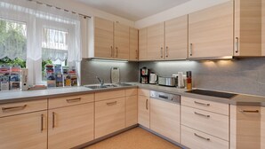 A modern kitchen with light wood cabinets, stainless steel appliances, and a window with sheer curtains. - Apartment "Völker" with Shared Garden & Wi-Fi (Haslach im Kinzigtal)