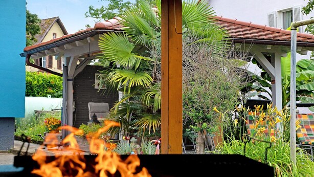 A garden with a fire pit, a wooden pergola, and various plants. - Apartment "Völker" with Shared Garden & Wi-Fi (Haslach im Kinzigtal)