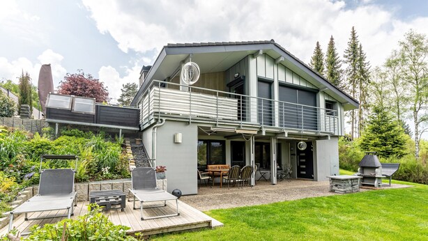 Een modern huis met twee verdiepingen, een balkon, zitplaatsen buiten en een barbecuehoek.