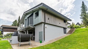 Een modern huis met twee verdiepingen, een balkon en een wentrap naar de bovenverdieping, plus een klein tuin.