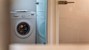 Voorzijde van een wasmachine in een kamer met een glazen deur en een witte muur.