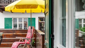 Una terraza de madera con una silla roja, un paraguas amarillo y una puerta verde.