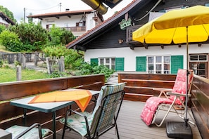 A wooden deck with a table and chairs, a yellow umbrella, and a building with green shutters in the background. - Renovated Apartment "Ferienwohnung - Hexi" with Mountain View, Private Terrace & Wi-Fi (Bad Kohlgrub)