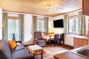 A cozy living room with a sofa, armchair, and table, a TV mounted on the wall, and a kitchen area with a sink and counter. - Renovated Apartment "Ferienwohnung - Hexi" with Mountain View, Private Terrace & Wi-Fi (Bad Kohlgrub)