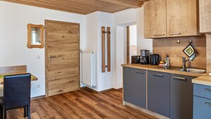 A kitchen with wooden cabinets, a countertop, a sink, and a dining area with a chair. - Renovared Apartment "Lengdobler - Leni" with Mountain View, Balcony & Wi-Fi (Bad Kohlgrub)