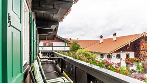 A balcony with wooden railings, a row of green-striped cushioned chairs, and a view of traditional buildings with red-tiled roofs. - Renovared Apartment "Lengdobler - Leni" with Mountain View, Balcony & Wi-Fi (Bad Kohlgrub)