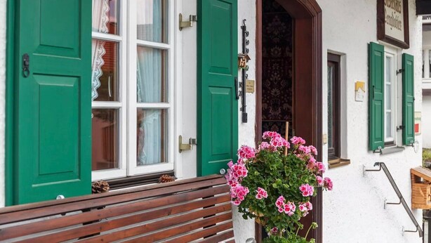A building with green shutters, a wooden bench, and a potted plant with pink flowers. - Renovared Apartment "Lengdobler - Leni" with Mountain View, Balcony & Wi-Fi (Bad Kohlgrub)