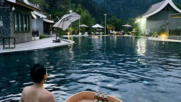A man in a swimming pool with a floating basket containing food and drinks. - Xaymone Riverside Resort and Restaurant (Vang Vieng)