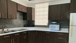 A modern kitchen with dark wooden cabinets, a white countertop, a stainless steel sink, and a microwave. - House near the beach 4B/2Bath (San Juan)