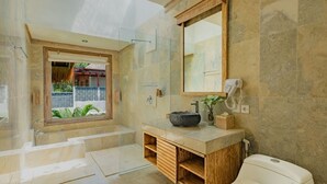 Un baño moderno con bañera, un espejo grande, un lavabo con lavamanos de piedra y un inodoro.