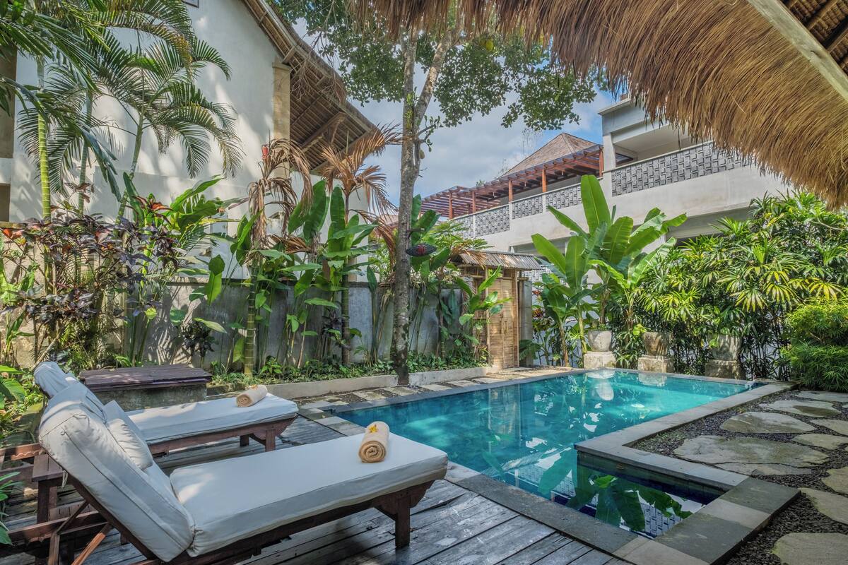 Área de piscina com espreguiçadeiras e plantas tropicais.