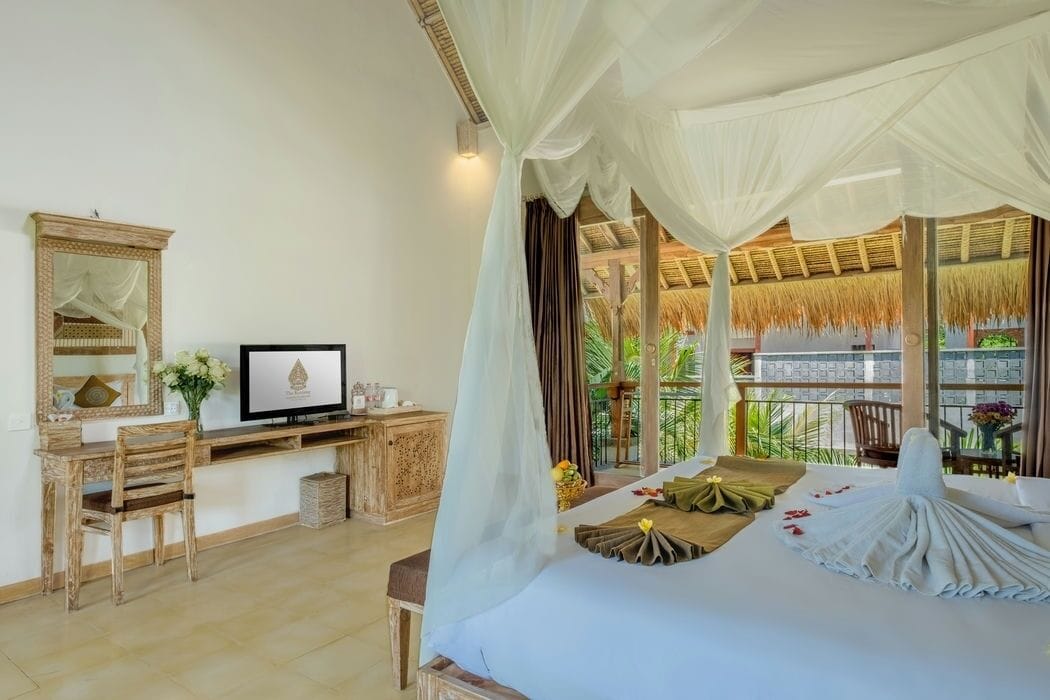 A bedroom with a bed, a desk, a chair, a TV, and a balcony with a thatched roof.