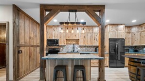 A kitchen with wooden cabinets, a central island with stools, a hanging light fixture, and a black refrigerator.