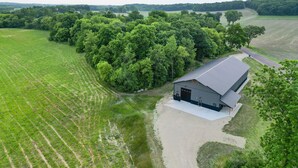 A large barn with a metal roof, surrounded by lush green fields and dense trees.