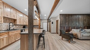 A modern kitchen with wooden cabinets, a central island with stools, and a dining area with a sofa and coffee table.