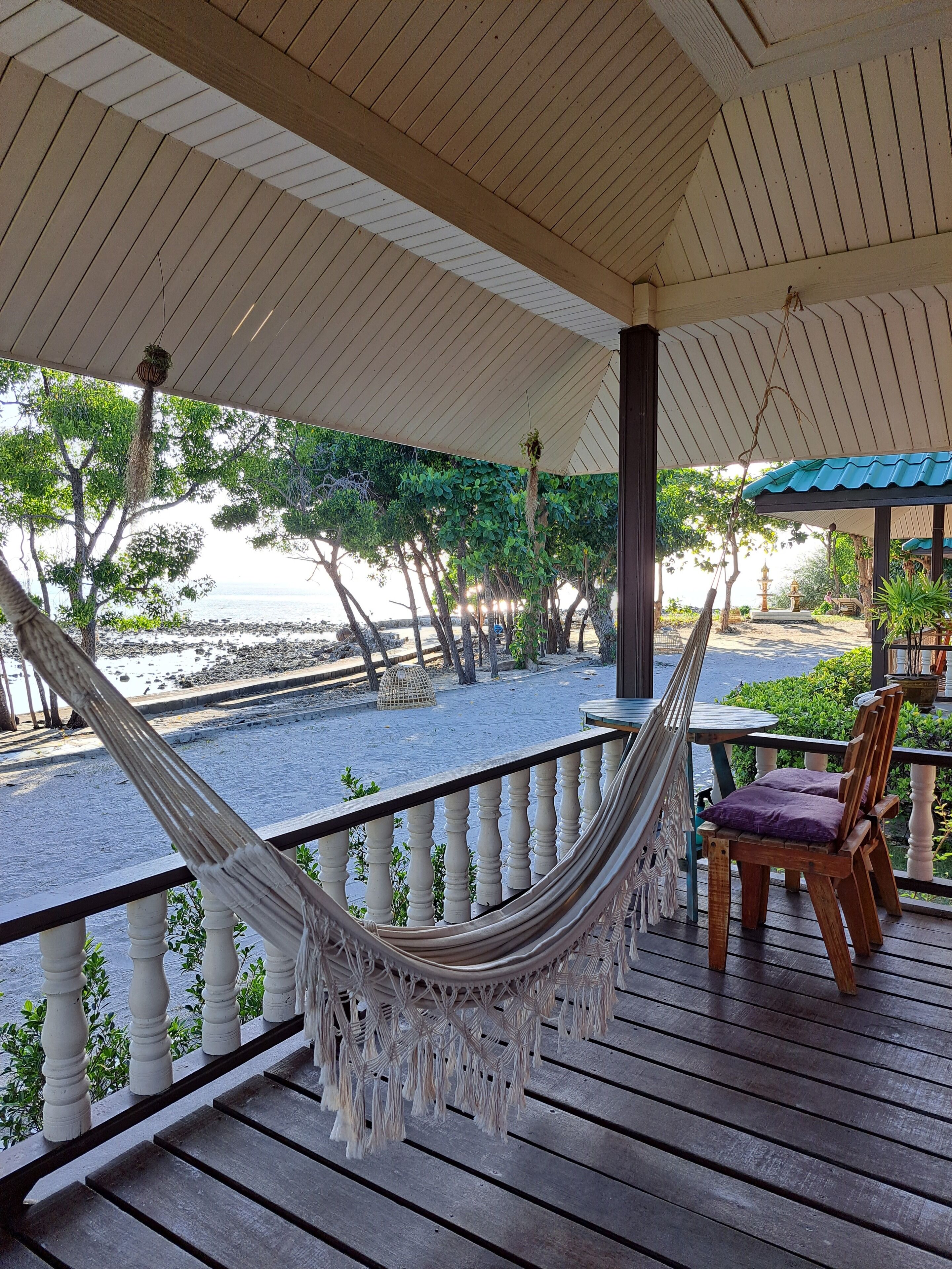 A wooden deck with a hammock, a table with chairs, and a view of the beach and ocean.